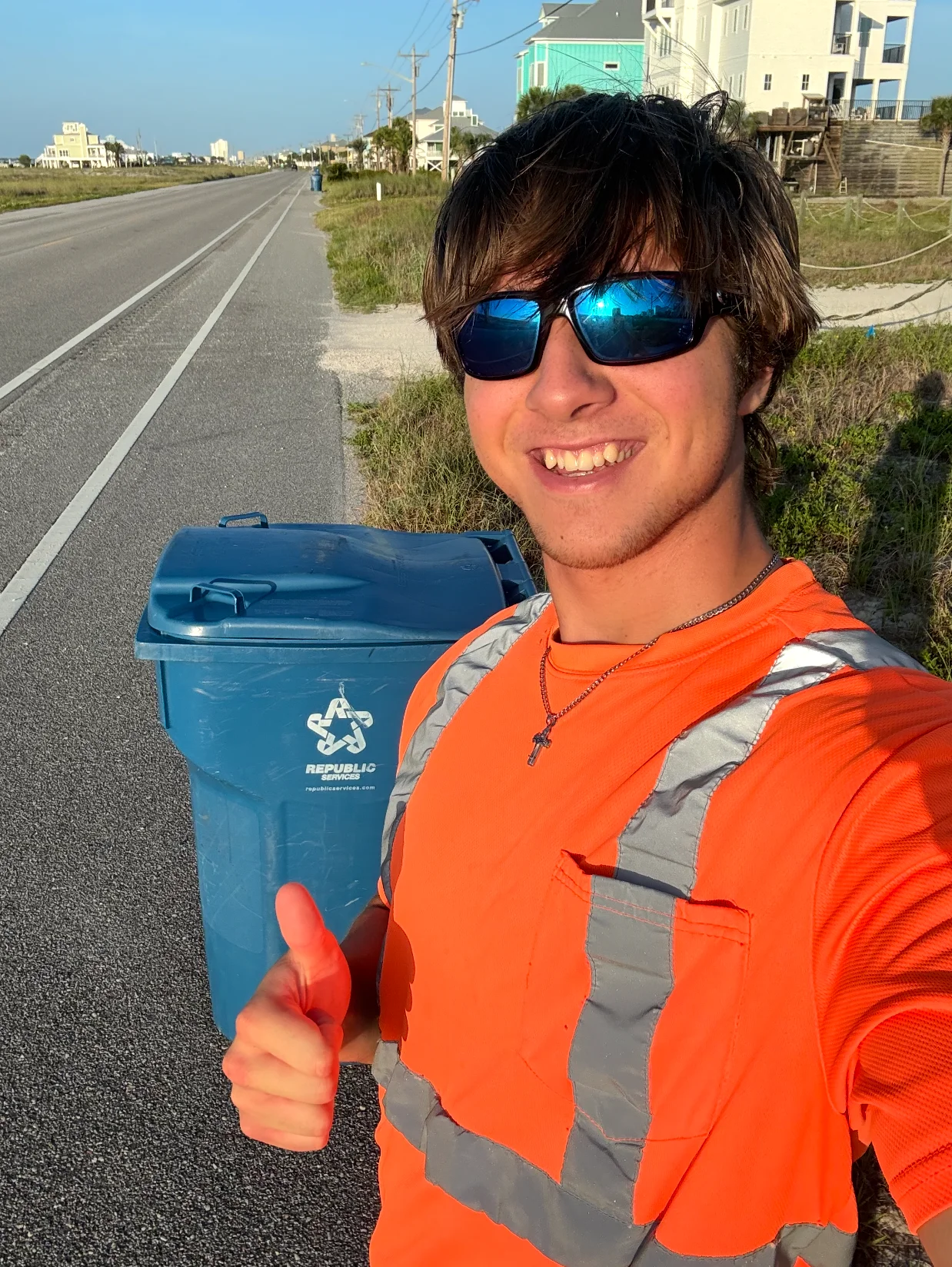 Ezekiel Vega in a safety shirt beside a recycling bin on a coastal can-to-curb route